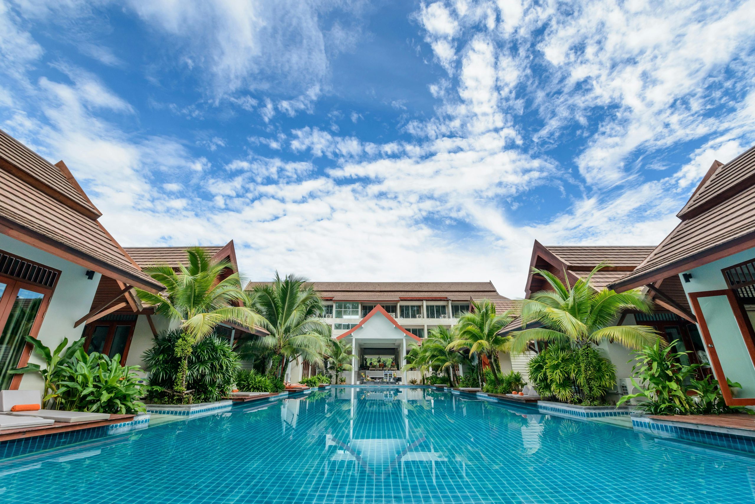 Spacious swimming pool surrounded by tropical villas under a bright blue sky, perfect for relaxation.