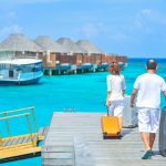 A couple arriving at a luxurious Maldives resort dock with luggage, capturing a tropical vacation vibe.