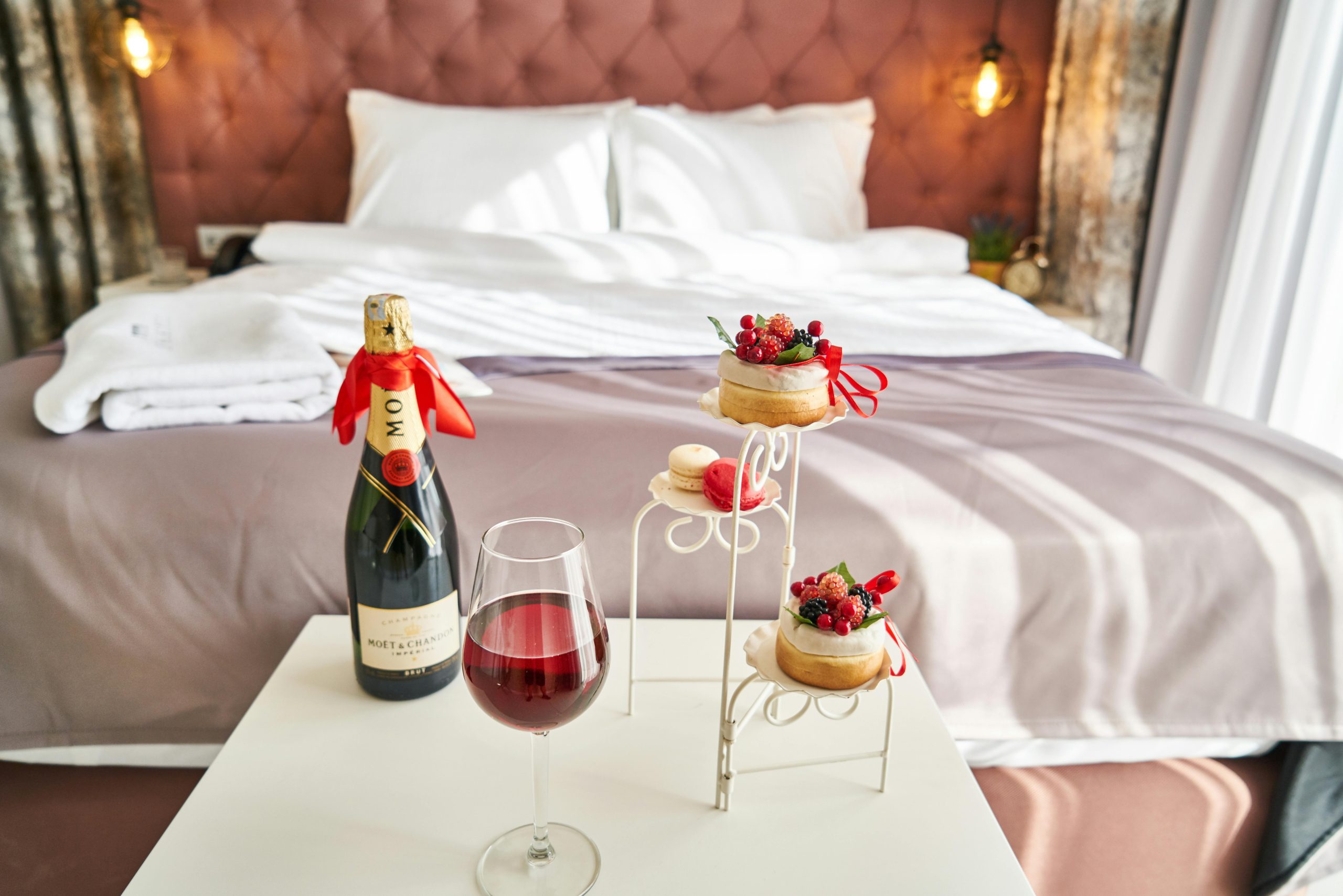 Elegant bedroom setting with champagne, wine glass, and desserts, creating a cozy ambiance.