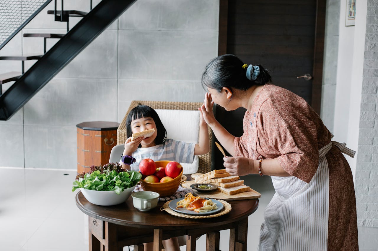 Asian grandmother and granddaughter sharing a joyful breakfast with toast and fruits indoors.