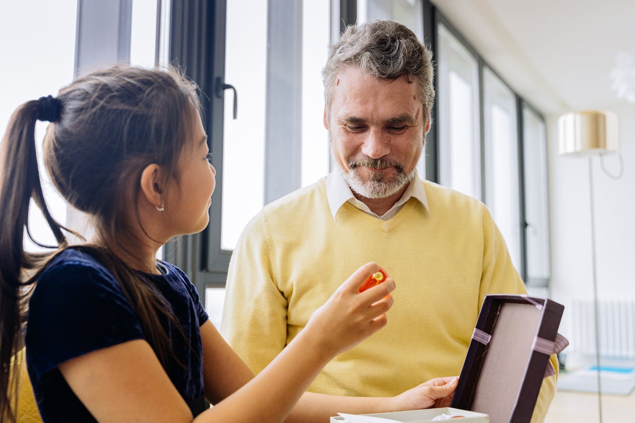 about-06 A cheerful elderly man receives a heartfelt gift from his granddaughter indoors.