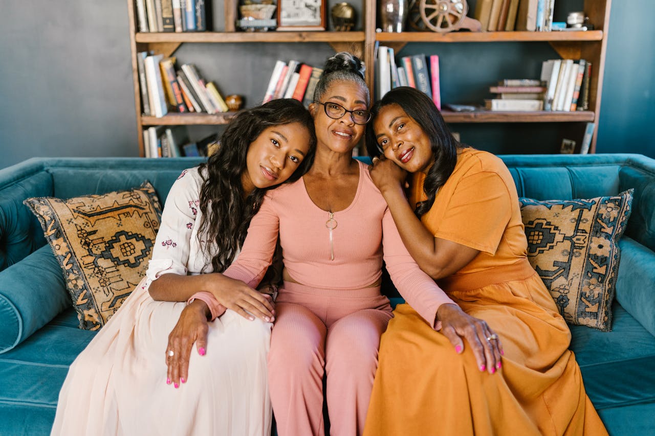 A joyful family moment shared by three African American women sitting on a sofa with a warm embrace.