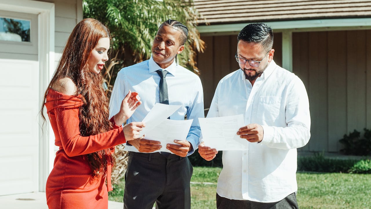 gallery-01 A diverse group evaluates real estate documents outside a residential property in daylight.