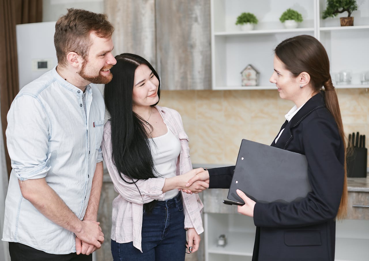 journey-01 A real estate agent greets a couple with a handshake in a modern home interior.