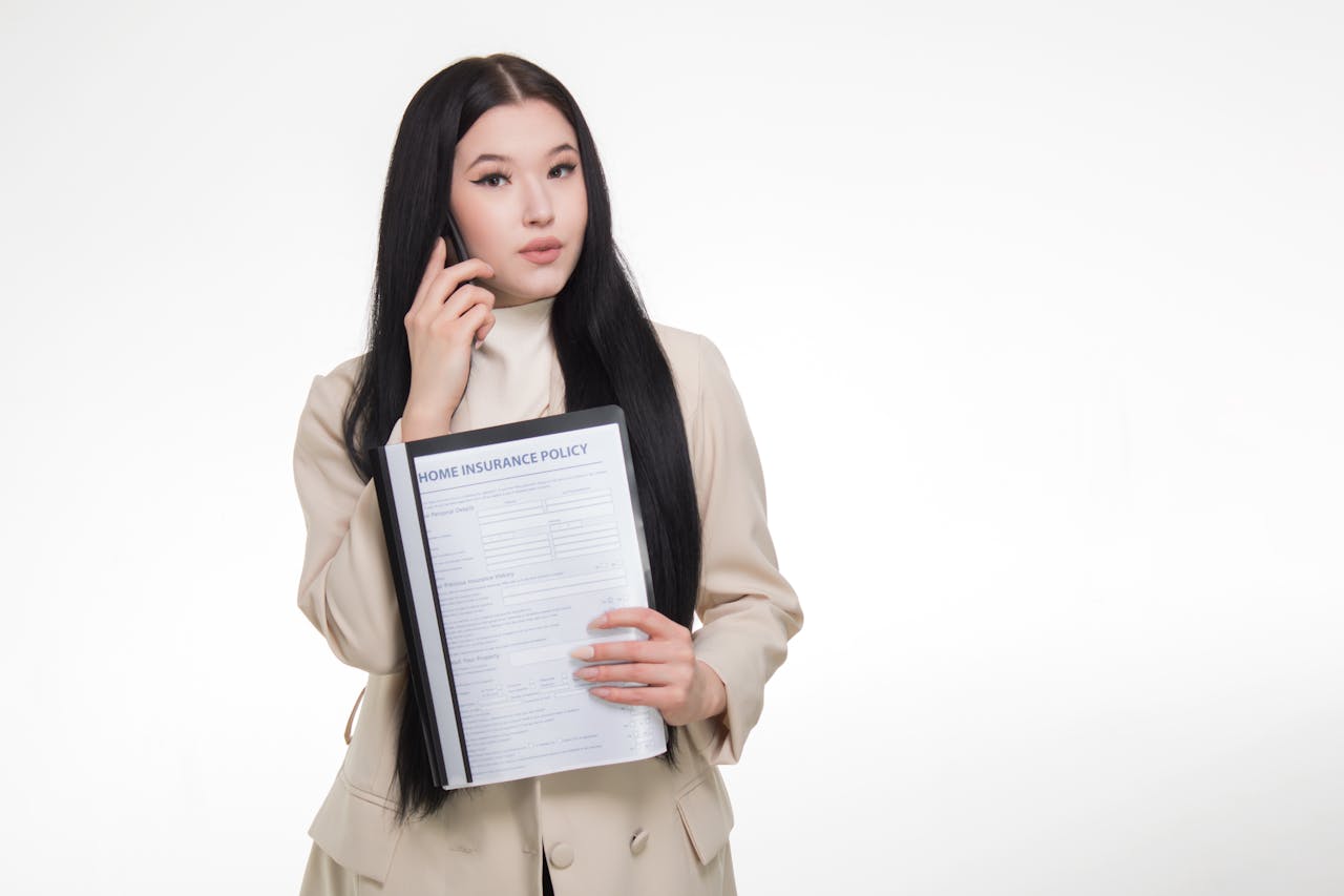 about-img Asian woman in business attire holding home insurance policy while on a phone call.