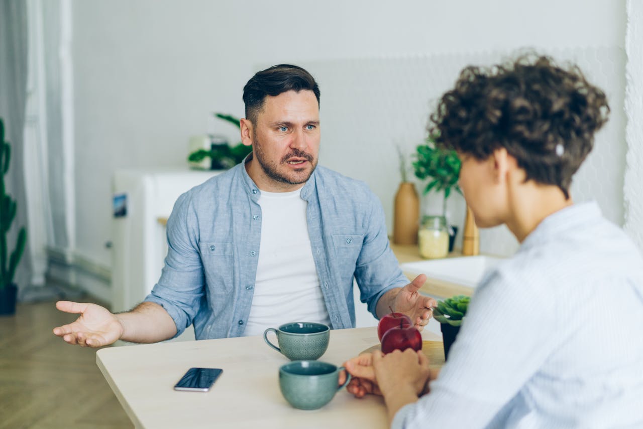 our-experience Two adults engage in a conversation at a kitchen table with coffee cups.