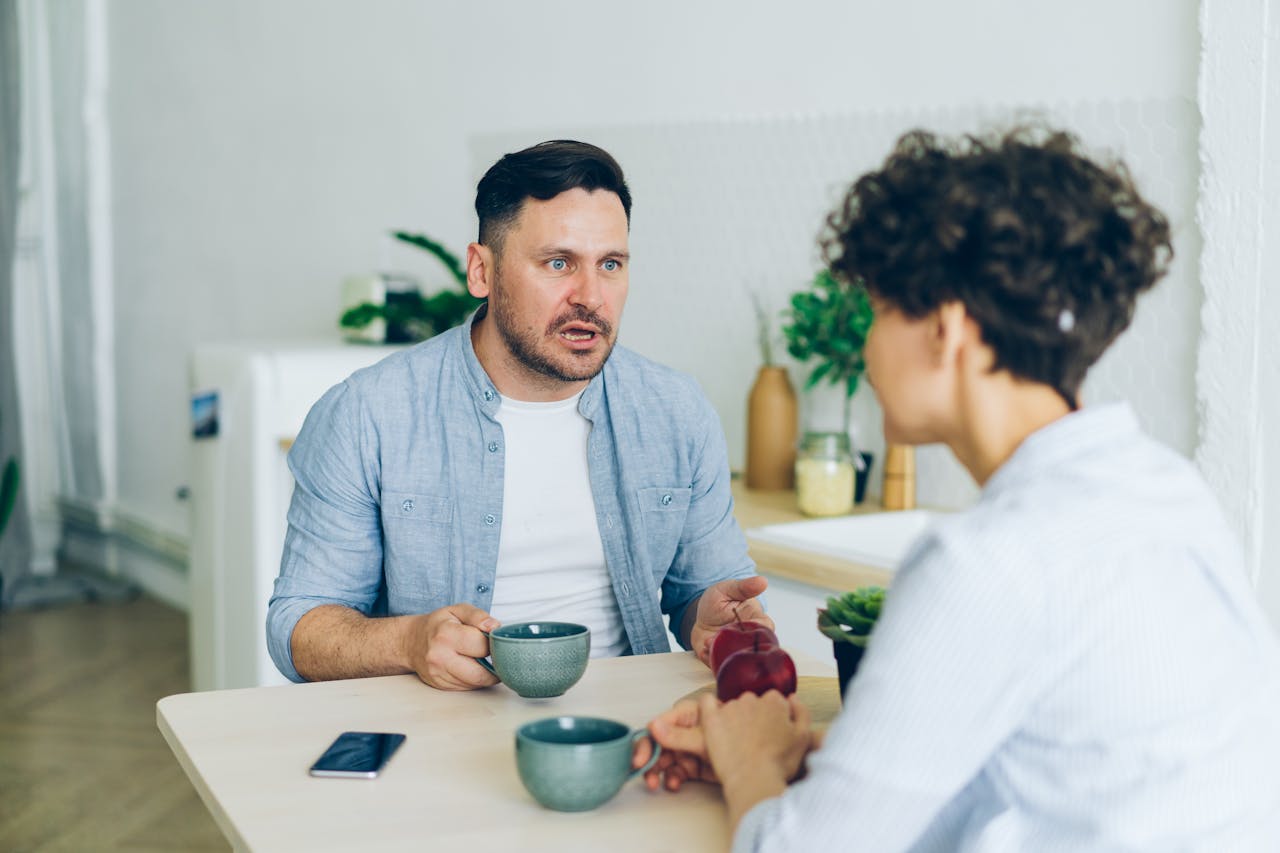 Couple having a serious conversation at the kitchen table with coffee cups.