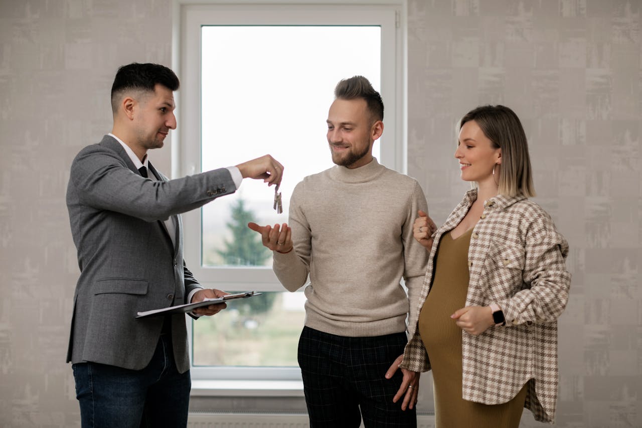 ours-journey A pregnant woman and her partner receive house keys from a real estate agent indoors.
