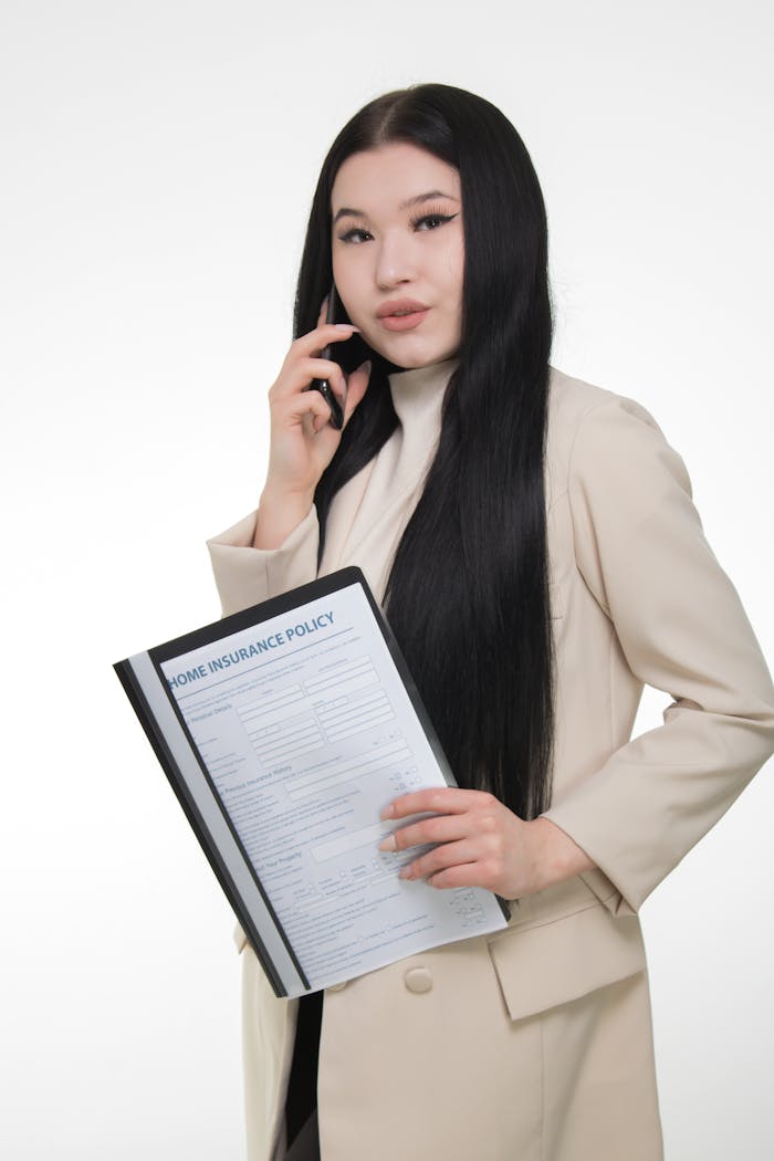 Confident woman in beige blazer holding a home insurance policy.